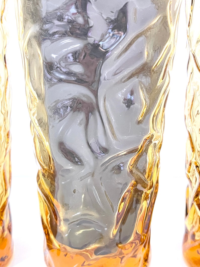 Op de afbeelding: Set van drie amberkleurige glazen met een getextureerd, geribbeld oppervlak. De glazen zijn helder en hebben een licht amberkleurige tint.
