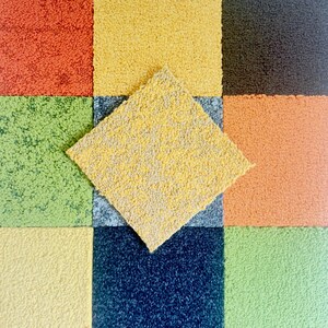 May include: A vibrant arrangement of carpet tiles in shades of yellow, orange, green, and blue. A yellow and grey tile is placed diagonally on top, creating a textured, geometric pattern. The tiles are likely for home decor.