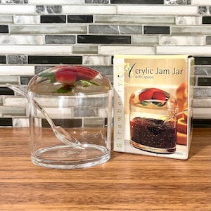 May include: Clear acrylic jam jar with a lid and a spoon. The jar is filled with red jam and has a strawberry on top of the lid. The box says "Acrylic Jam Jar with spoon".