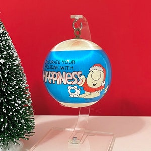 May include: A blue and white Christmas ornament with a cartoon character and the text "Decorate your holiday with happiness".