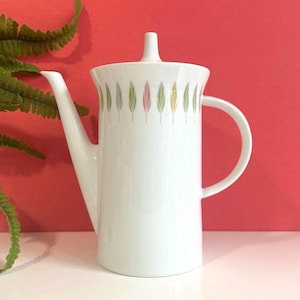 May include: White ceramic coffee pot with a lid and a handle. The pot features a design of colourful leaves around the middle.