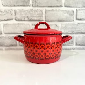 Peut inclure: Une marmite en émail rouge vif avec un couvercle assorti et deux poignées latérales. L'extérieur présente un motif géométrique répétitif de cercles floraux rouge foncé et orange entourant le corps de la marmite avec un bord noir.