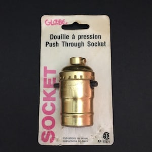 May include: A gold-coloured push-through light bulb socket packaged on a white card with the text "GLOBE Douille à pression Push Through Socket SOCKET Indications au verso Instructions on back AP 57271".