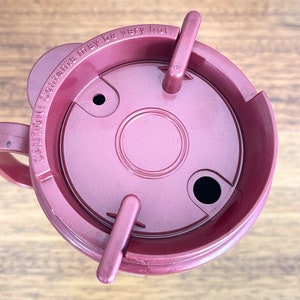 May include: A maroon travel mug with a lid that has a warning label that reads "CAUTION: Contents may be very hot."
