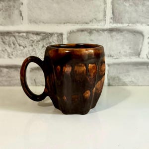 May include: A brown ceramic mug with a textured, mottled glaze. The mug has a rounded body and a handle.