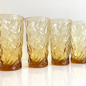 Op de afbeelding: Set van vier amberkleurige glazen met een getextureerd, boomvormig ontwerp. De glazen zijn helder en hebben een licht amberkleurige tint.