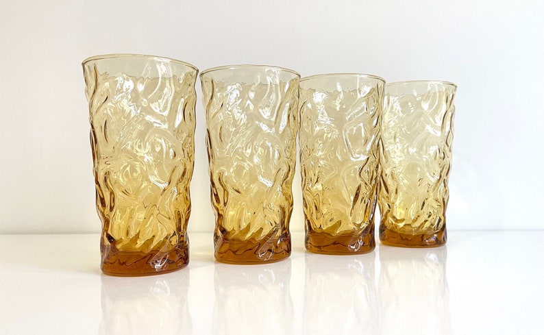 Op de afbeelding: Set van vier amberkleurige glazen met een getextureerd, boomvormig ontwerp. De glazen zijn helder en hebben een licht amberkleurige tint.