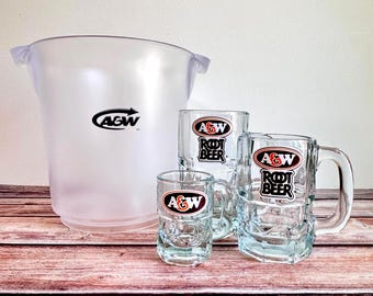 May include: A clear plastic ice bucket and three glass mugs with the A&W Root Beer logo. The mugs are different sizes, with handles and a textured design. The ice bucket has the A&W logo.