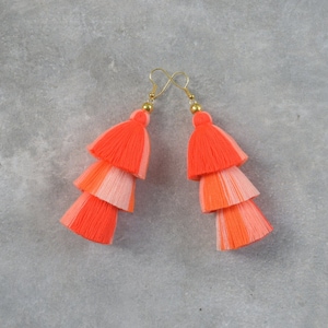 May include: A pair of coral and pink tassel earrings with gold hooks. The tassels are layered in three tiers.