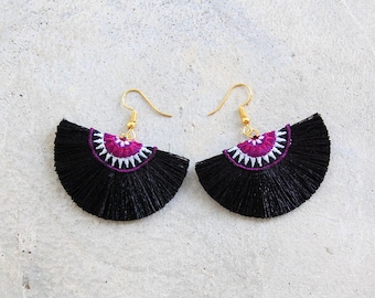 May include: A pair of black tassel earrings with a pink and white embroidered design.