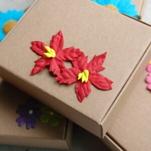 May include: Two brown cardboard boxes with red paper flowers on top. The boxes are stacked on top of each other. The flowers have yellow centers.