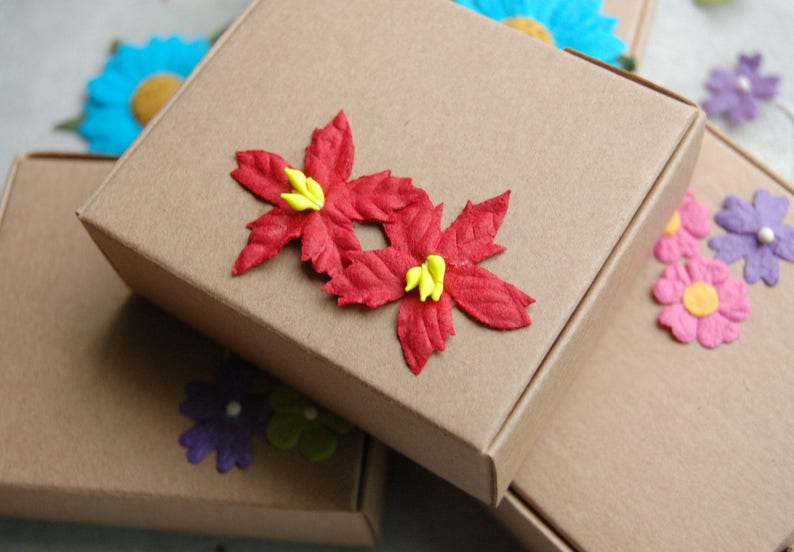 May include: Two brown cardboard boxes with red paper flowers on top. The boxes are stacked on top of each other. The flowers have yellow centers.