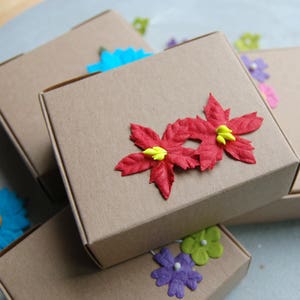Puede incluir: Pila de cajas de cart&oacute;n marr&oacute;n decoradas con flores de papel rojo, amarillo y azul. Las cajas est&aacute;n apiladas unas sobre otras.