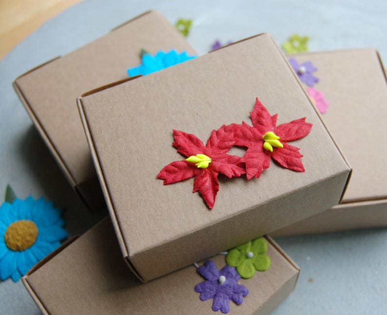 Puede incluir: Pila de cajas de cart&oacute;n marr&oacute;n decoradas con flores de papel rojo, amarillo y azul. Las cajas est&aacute;n apiladas unas sobre otras.