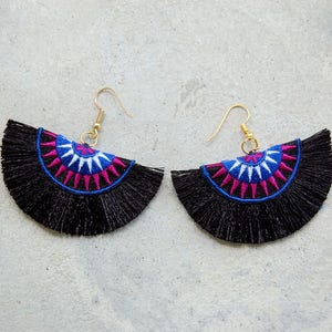 May include: A pair of black tassel earrings with a colorful geometric design. The earrings feature a semi-circle shape with a pink, blue, and white pattern.