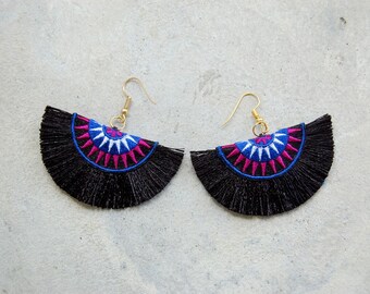May include: A pair of black tassel earrings with a colorful geometric design. The earrings feature a semi-circle shape with a pink, blue, and white pattern.