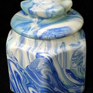 May include: A ceramic jar with a lid, featuring a swirling blue and white marbled design. The jar has a square base and a rounded lid.