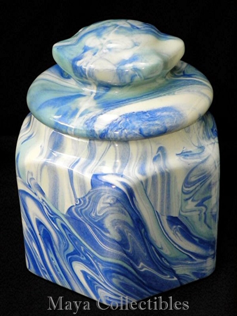 May include: A ceramic jar with a lid, featuring a swirling blue and white marbled design. The jar has a square base and a rounded lid.