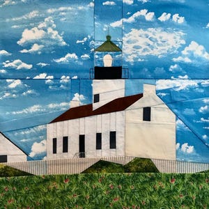 Könnte beinhalten: Ein Textilkunstwerk, das einen weißen Leuchtturm mit braunem Dach und schwarzen Fenstern zeigt. Der Leuchtturm ist vor einem blauen Himmel mit flauschigen weißen Wolken platziert. Grünes Gras und ein weißer Zaun befinden sich im Vordergrund.