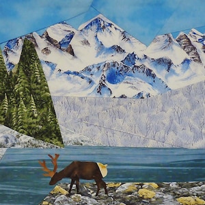 May include: A mixed media artwork depicting a mountain landscape with snow-capped peaks, a lake, and a reindeer. The artwork features a collage style with geometric shapes and a color palette of blues, greens, and browns. The reindeer is brown with large antlers.