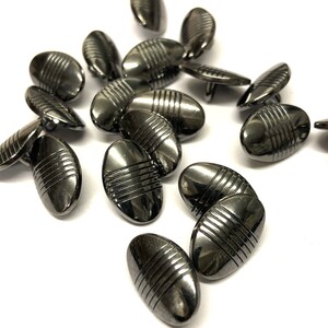 May include: A group of 16 black oval buttons with a silver metallic finish and a grooved design.