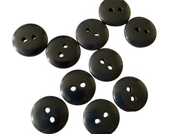 May include: A collection of ten black, round buttons with two holes each. The buttons are made of a smooth, glossy material and are evenly spaced against a white background. These buttons are suitable for sewing and craft projects.