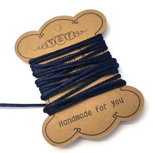 Può includere: Un rocchetto di cordoncino blu navy avvolto attorno a un'etichetta di cartoncino marrone con il testo "Handmade for you".