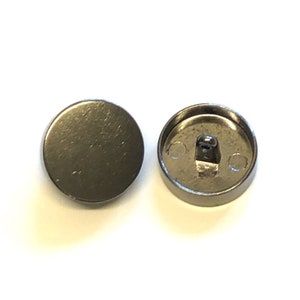 May include: Two silver-toned round buttons with a shank on the back. The buttons are smooth and have a slightly textured surface.
