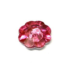 Puede incluir: Un botón rosa en forma de flor con un centro transparente y un diseño facetado.