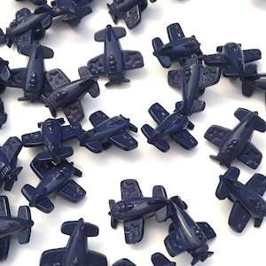 Peut inclure: Une collection de boutons en plastique bleu marine en forme d'avion. Chaque bouton présente un motif d'étoile et une forme d'avion détaillée.