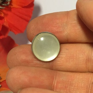 May include: A white oval-shaped button with a silver metal rim. The button has a smooth, glossy finish.