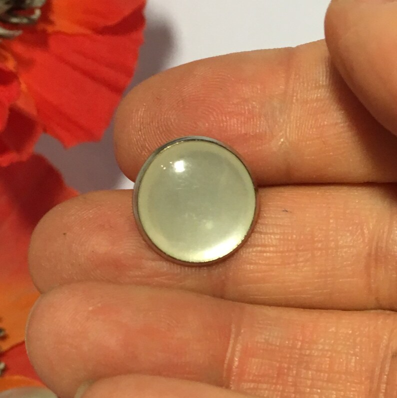 May include: A white oval-shaped button with a silver metal rim. The button has a smooth, glossy finish.