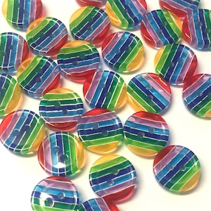 Op de afbeelding: Een verzameling kleurrijke regenboog gestreepte knopen. De knopen zijn gemaakt van helder plastic met een regenboog streep ontwerp. De knopen zijn tweegaats.
