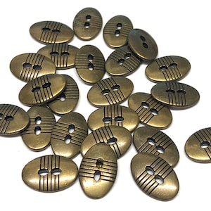 May include: A collection of 20 oval-shaped metal buttons with a gold finish. Each button has two holes and a decorative etched design of horizontal lines.
