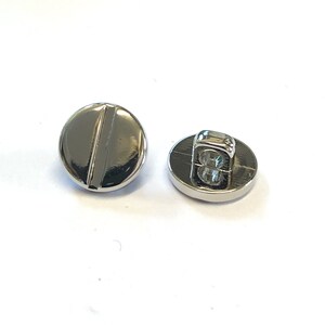 May include: Two silver metal buttons, one with a shank and the other with a flat back. The button with the shank has a groove running down the centre.