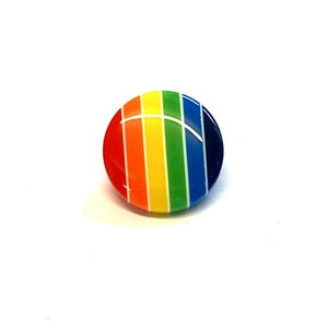 May include: A round, rainbow-coloured button with a glossy finish. The button has stripes of red, orange, yellow, green, blue, and purple.