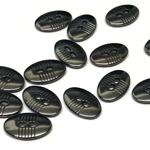 May include: A group of 12 oval-shaped buttons with a metallic finish. The buttons have a black color and a raised design of two holes and three lines.