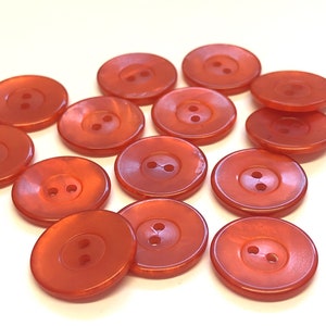 May include: A collection of 12 orange plastic buttons, each with two holes. The buttons are round and have a glossy finish.