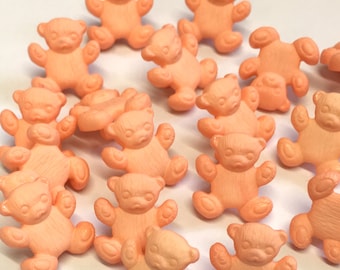 May include: A collection of peach-colored plastic teddy bear buttons. The buttons are about 1 inch in diameter and have a flat back.