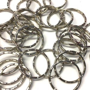 May include: A pile of silver-toned metal key rings. The key rings are all the same size and have a textured finish.