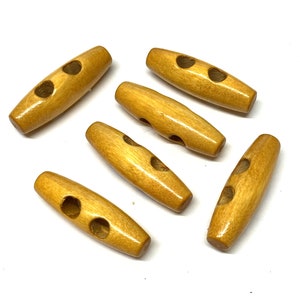 May include: Six wooden toggle buttons, each with two holes. The buttons are a light brown colour and have a smooth, polished finish.