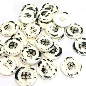 May include: A pile of white buttons with black brushstrokes. The buttons have four holes each.