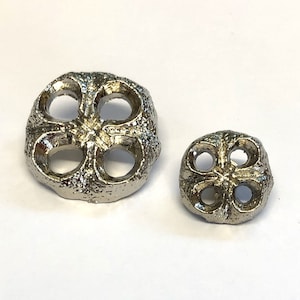 Op de afbeelding: Twee zilveren metalen knopen met een klaverbladontwerp. De grotere knop is ongeveer 5 cm in diameter en de kleinere knop is ongeveer 2,5 cm in diameter.