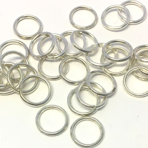 May include: A pile of silver jump rings, a type of metal ring used in jewelry making.