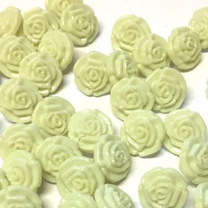 Peut inclure: Un ensemble de boutons en plastique de couleur jaune pâle en forme de roses. Les boutons sont disposés de manière aléatoire sur une surface blanche.