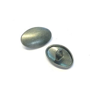May include: Two oval-shaped metal buttons with a silver finish. One button has a loop on the back for sewing.