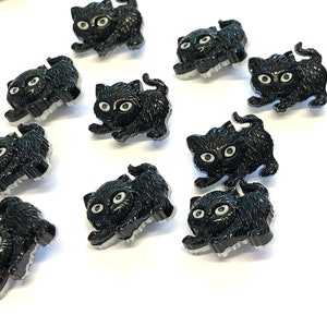May include: A collection of black plastic buttons shaped like kittens. The buttons have white eyes and are perfect for adding a whimsical touch to crafts and sewing projects.