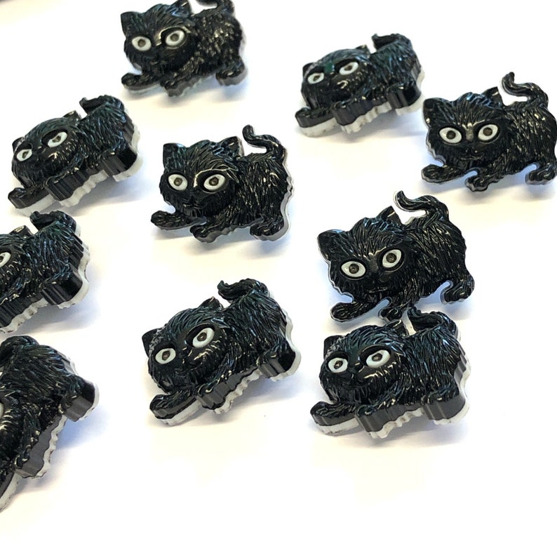 May include: A collection of black plastic buttons shaped like kittens. The buttons have white eyes and are perfect for adding a whimsical touch to crafts and sewing projects.