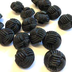 Puede incluir: Una colección de botones negros con un diseño tejido. Los botones son redondos y tienen una superficie texturizada en relieve.