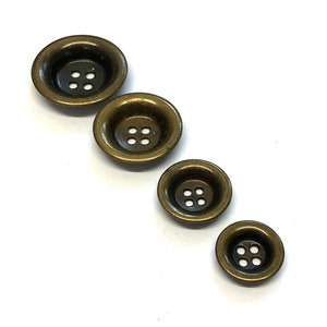 Pode incluir: Quatro botões de metal dourados com quatro furos cada. Os botões estão dispostos em linha do maior para o menor.